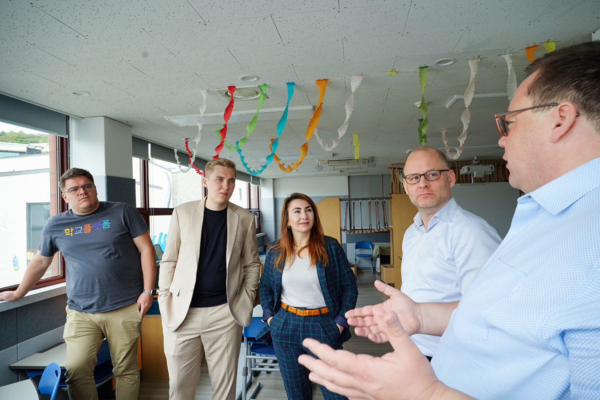 Das IServ-Team steht zusammen mit Schulleiter Robert Lengler in einem Klassenzimmer. Sie sprechen miteinander.