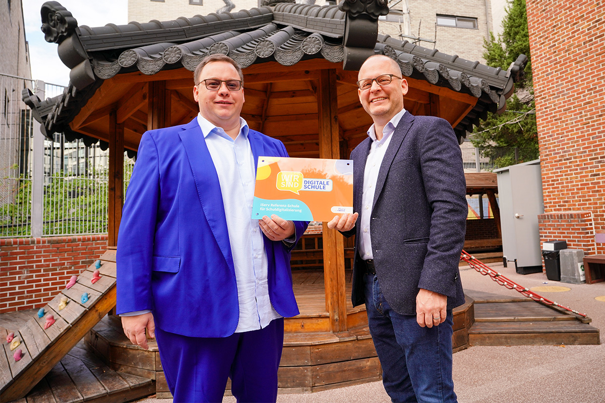 IServ-Geschäftsführer Benjamin Heindl und Schulleiter Robert Lengler stehen nebeneinander. Sie halten eine Plakette mit dem Aufdruck, auf der steht: Wir sind Digitale Schule.