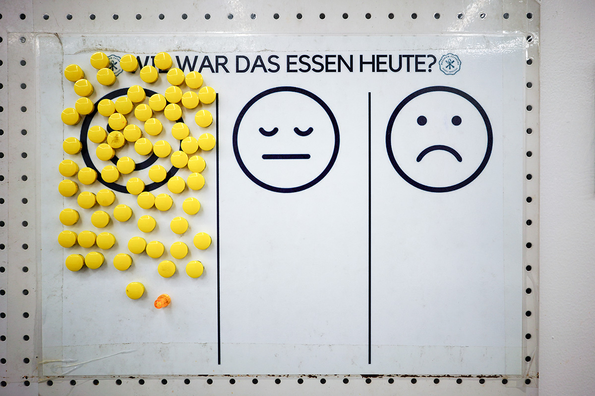 Ein Schild, auf dem steht: Wie war das Essen heute? Darunter sind drei Smileys abgebildet. Auf dem glücklichen Smiley sind viele gelbe Magnete.